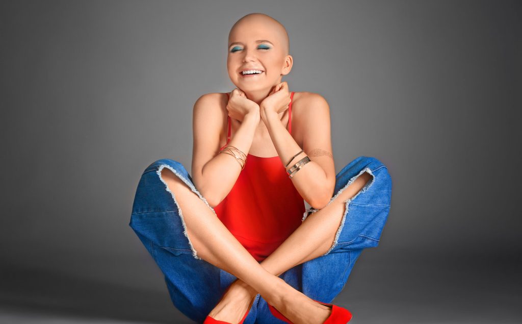 Beautiful bald woman sitting against grey background